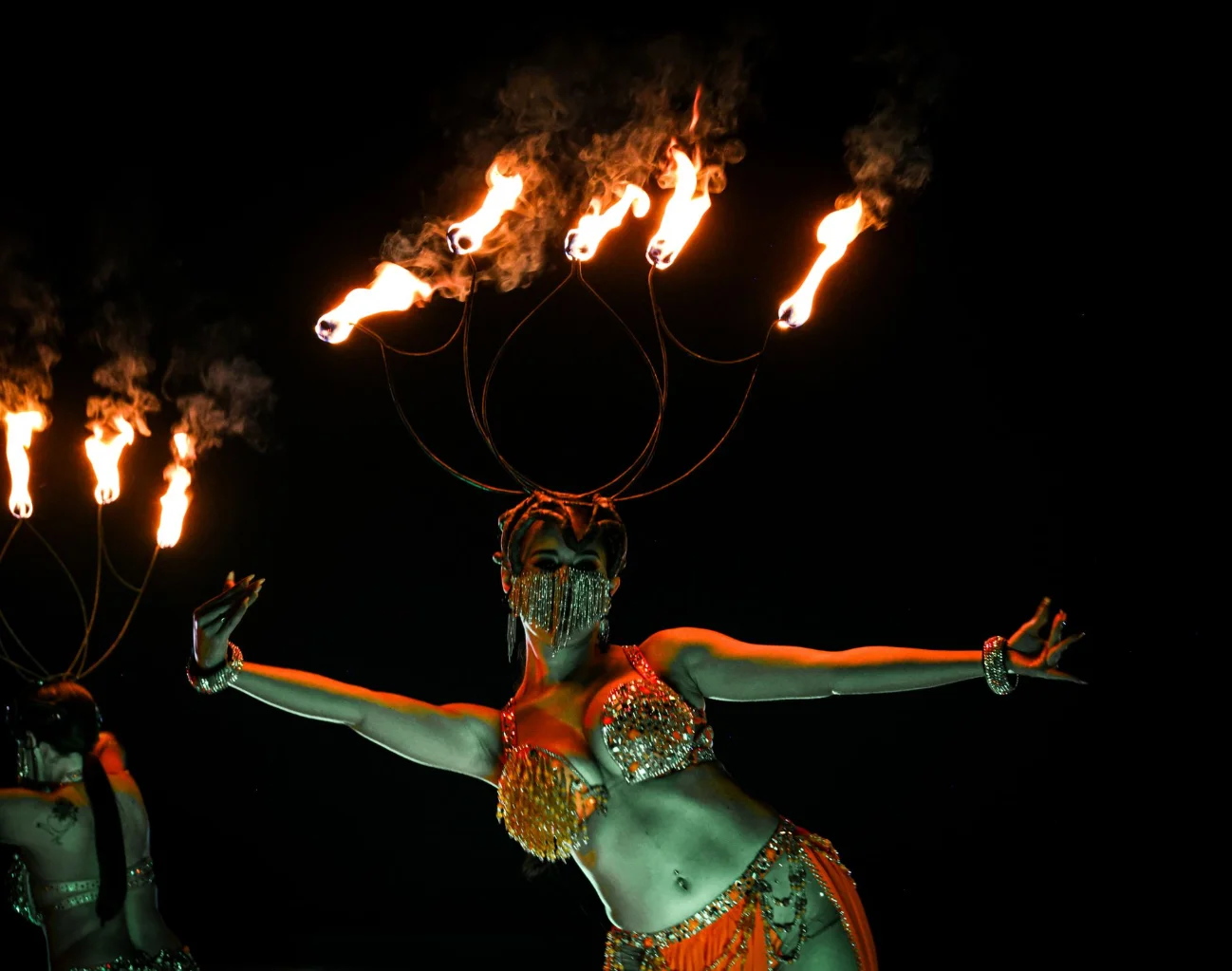 Costumed fire dancer with a flaming headpiece performing at night