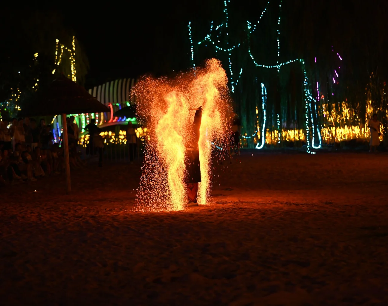 Fire show at an outdoor night venue with lights and guests
