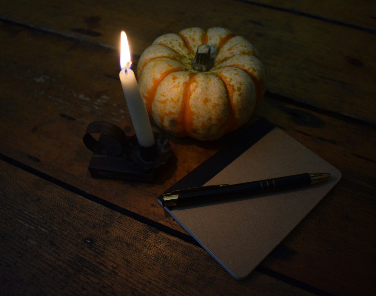 Notebook and pen next to a pumpkin and candle for planning a Halloween party in Dubai